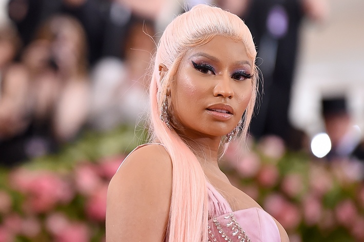 Nicki Minaj at a public event, wearing a beaded, elegant gown with her pink hair styled straight and long. She poses confidently for the camera