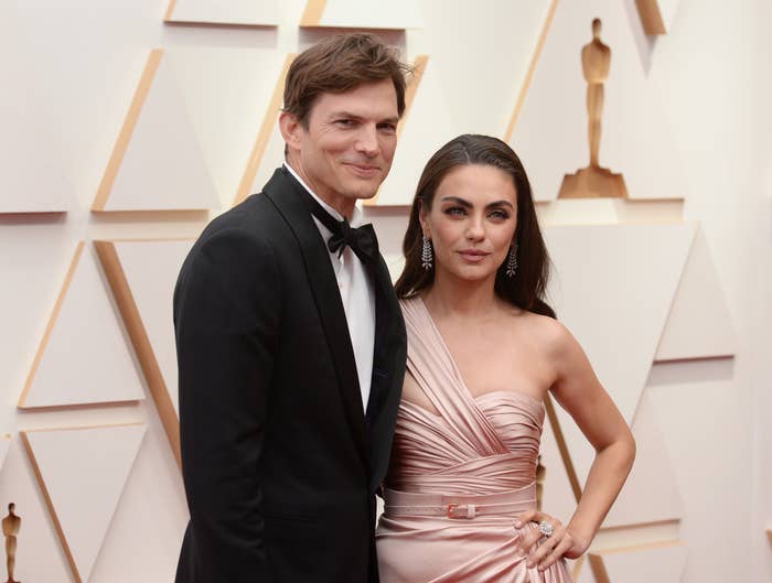 Ashton Kutcher in a suit and Mila Kunis in an elegant gown pose together on the red carpet at an awards event