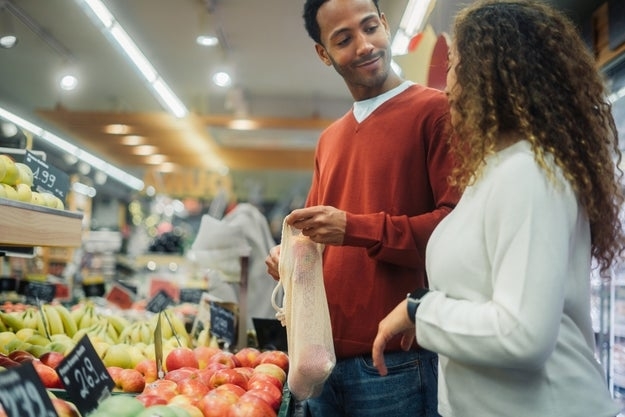 A man and a woman smile at each other while shopping for produce in a grocery store