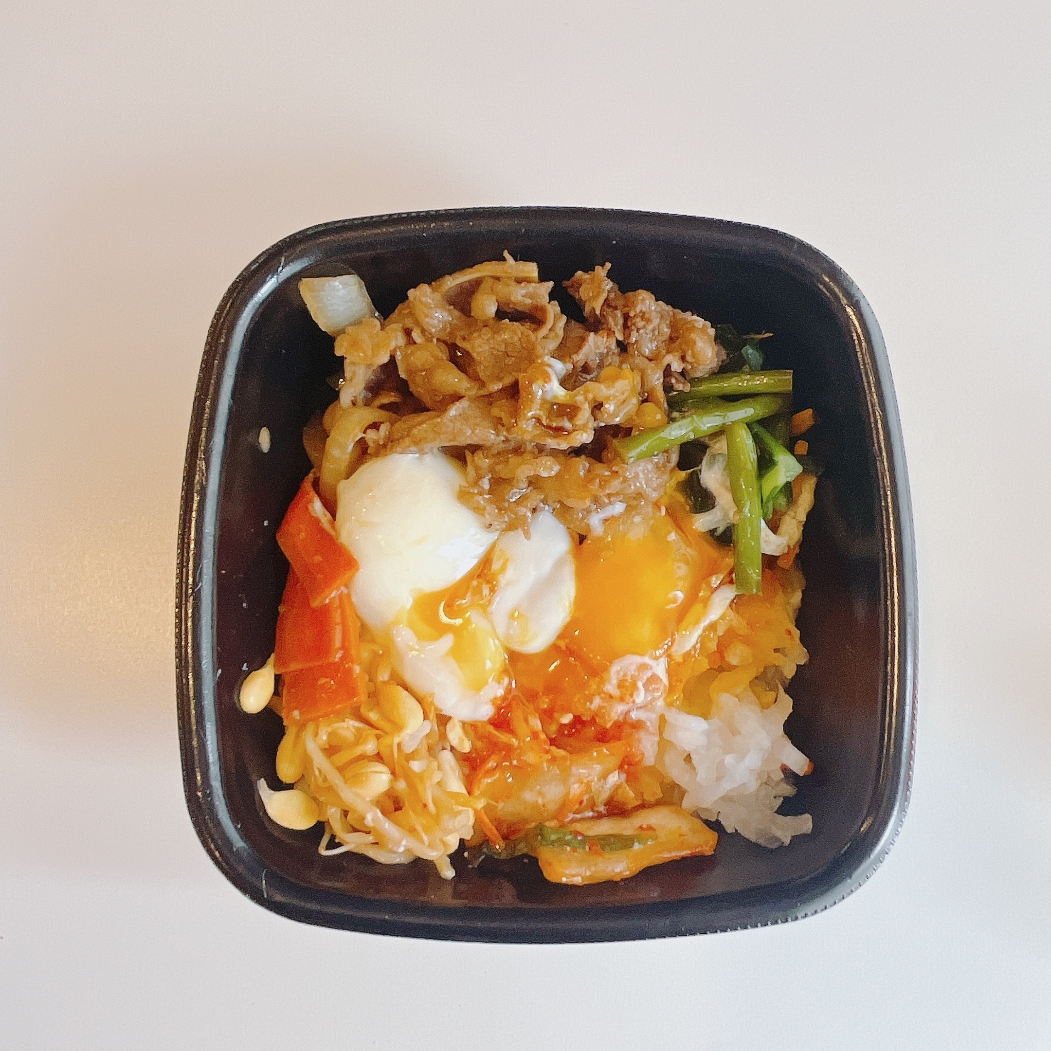黒い容器に盛られた混ぜご飯。目玉焼き、肉、野菜、キムチなどがトッピングされています。