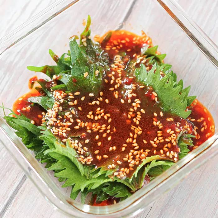 ガラス容器に盛られた大葉と特製のタレがかかった料理。タレにはゴマが散らされています。