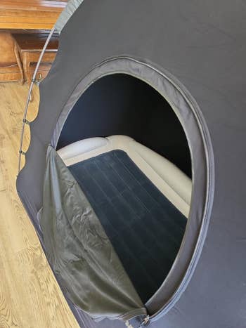 Tent with a zippered opening revealing an inflatable furniture inside, acceptable up successful a country with woody flooring