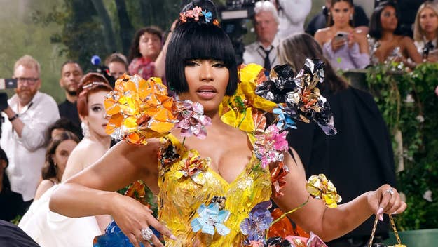 Nicki Minaj attending an event in a bold, floral-themed outfit adorned with colorful, sculpted flowers. Photographers and other guests in the background