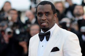 Sean "Diddy" Combs in a white tuxedo jacket with a black bow tie at a formal event, with photographers in the background