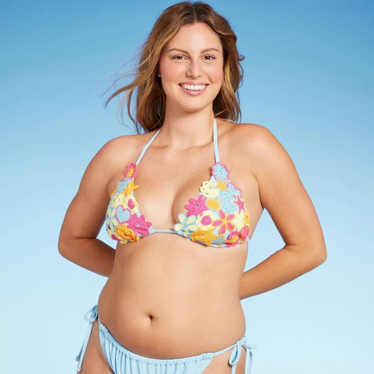 Seorang wanita mengenakan bikini bermotif bunga, tersenyum percaya diri dengan latar belakang polos