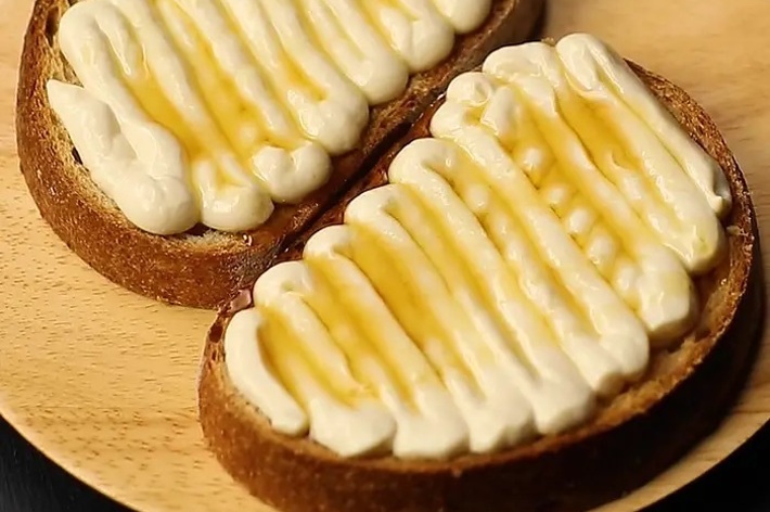 木のプレートに乗せられた2枚のトースト、それぞれにクリームとハチミツがかかっている。