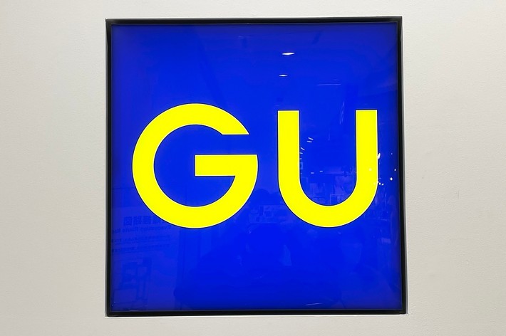 Artwork with the letters &ldquo;GU&rdquo; prominently displayed on a blue background, hung on a white wall