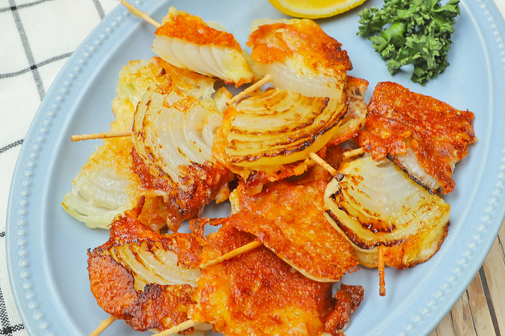 タマネギフライが串に刺されてお皿に盛りつけられている。隣にはレモンのくし切りとパセリの飾りが添えられている。