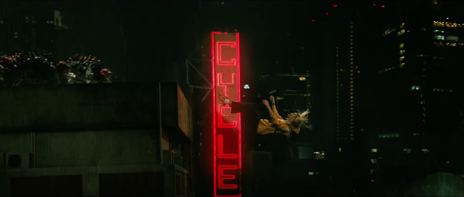 Blond person in yellow clothing is seen mid-air, seemingly falling or jumping off a building at night with a neon red &quot;CYCLE&quot; sign in the background amidst a cityscape