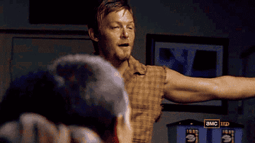 A man, potentially a character from AMC's &quot;The Walking Dead,&quot; in a sleeveless top with arms outstretched, addressing another character facing away
