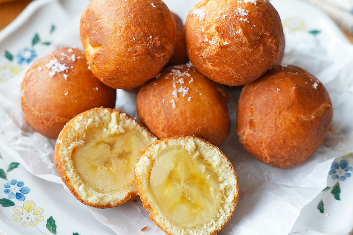 バナナフィリングが入った丸い揚げパンが白い紙とお皿の上に積み重ねられている。