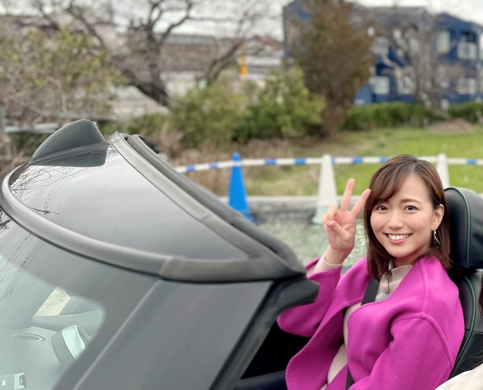 オープンカーに乗り、ピースサインをして微笑んでいる女性。
