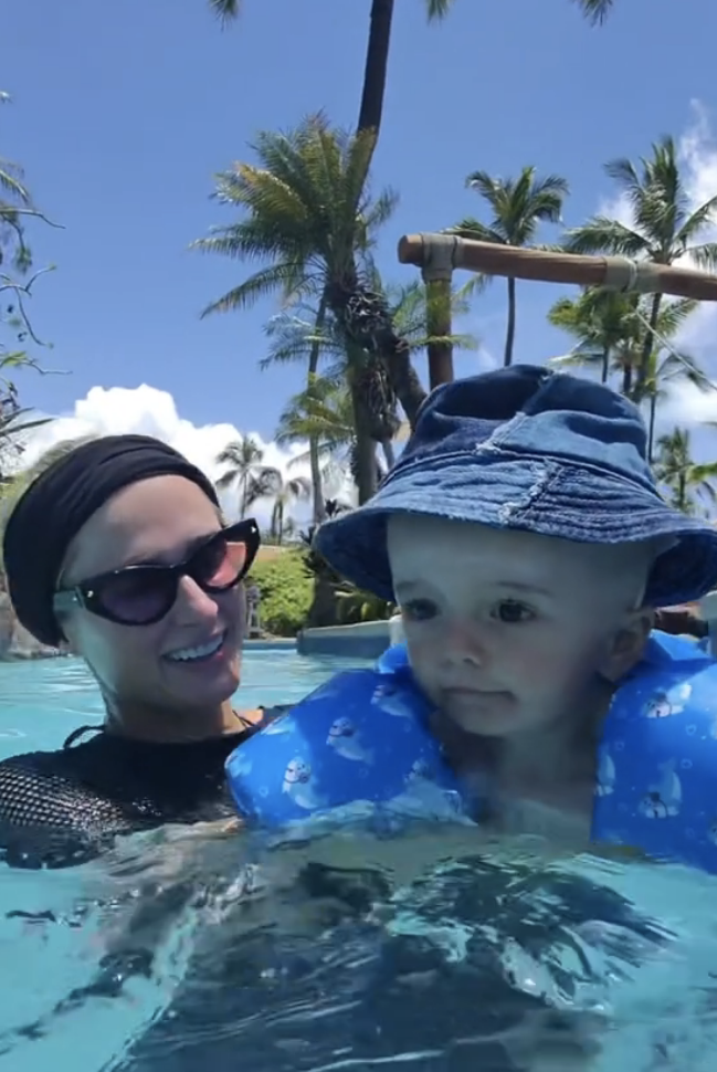 Paris Hilton is swimming in a pool with her baby who is wearing a sunhat