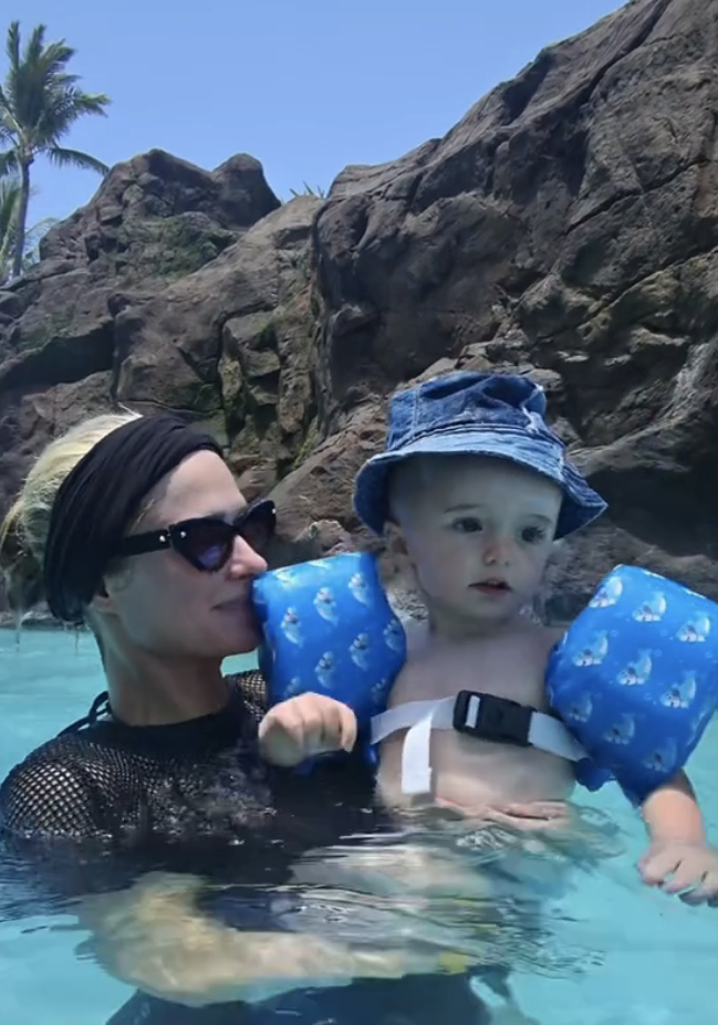 Paris Hilton is in a swimming pool holding a baby wearing arm floaties