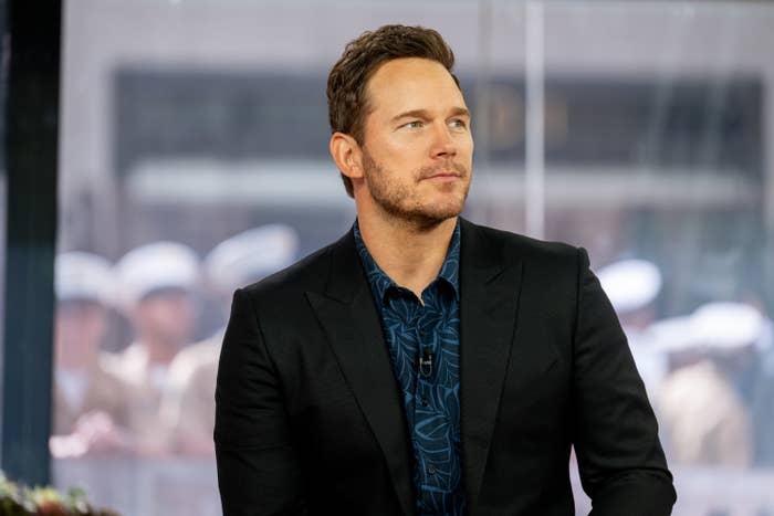 Chris Pratt, wearing a dark suit with a patterned shirt underneath, seated for an interview