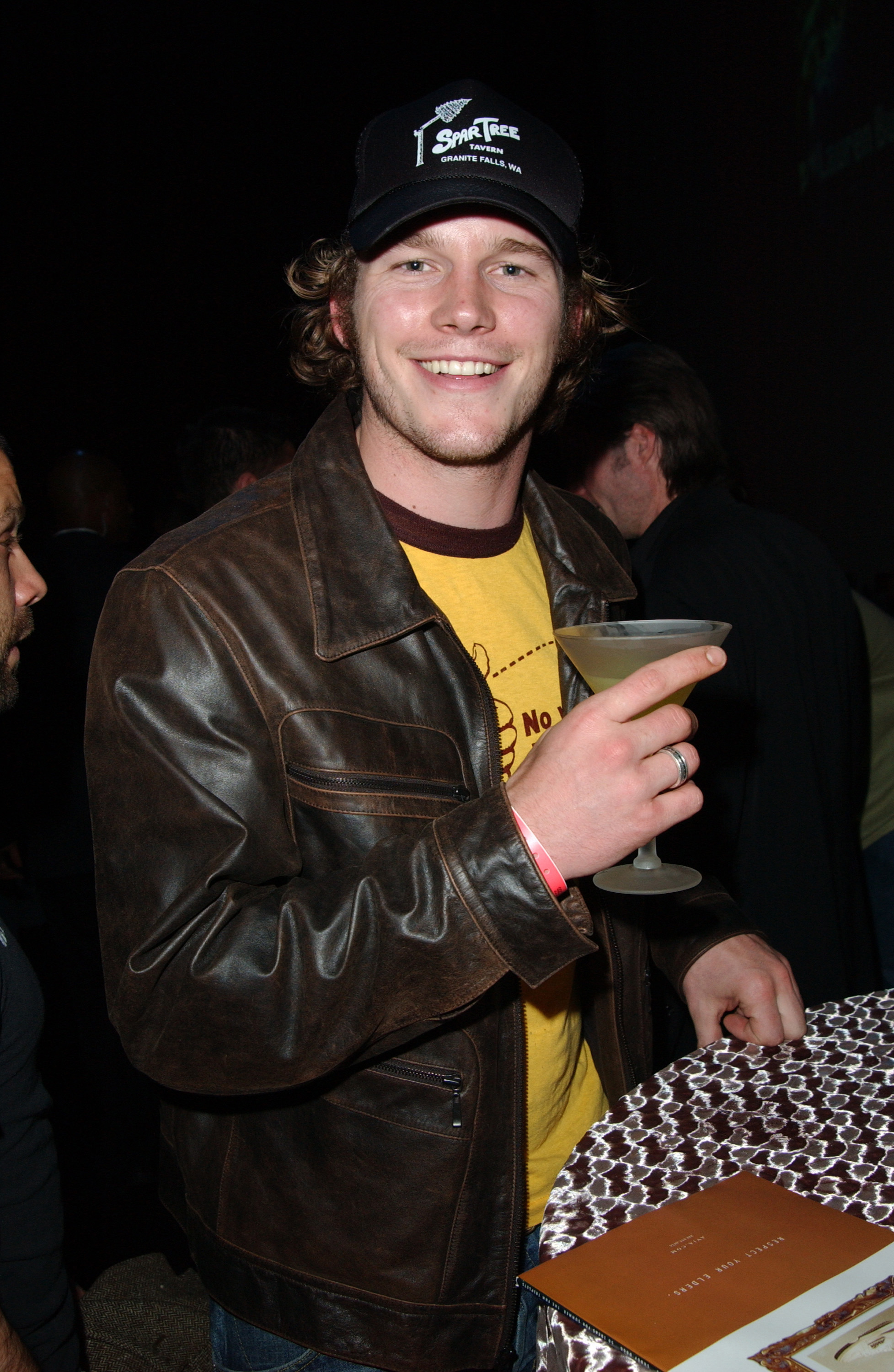 Chris Pratt, smiling and holding a drink at a table