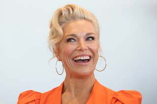 Hannah Waddingham smiling, wearing a stylish outfit with puffed shoulder sleeves and large hoop earrings