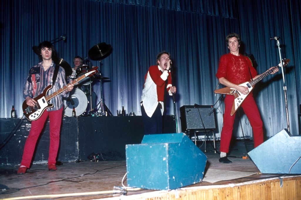Sid Vicious, Paul Cook, Johnny Rotten, and Steve Jones of the Sex Pistols performing on stage. Johnny Rotten is singing into the microphone