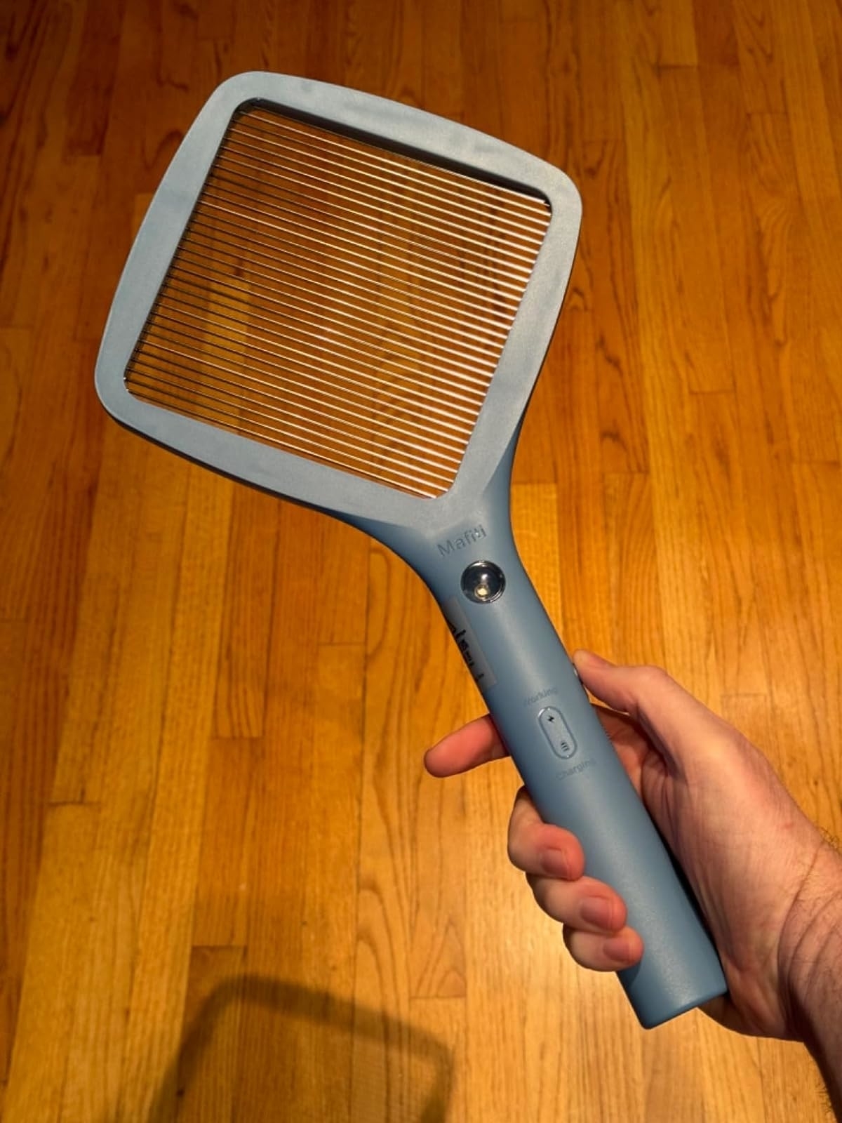 Reviewer holding a blue electric bug zapper with a wooden floor in the background