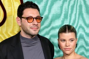 Sofia Richie on left with hair in a bun and diamond earrings; Elliot Grainge on right in glasses and black jacket