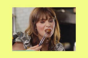 Zooey Deschanel eating food with chopsticks. She is wearing a patterned blouse
