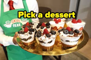 A person wearing a "Central Perk" apron holds a tray with multiple dessert cups topped with berries and chocolate. Text on the image says, "Pick a dessert."