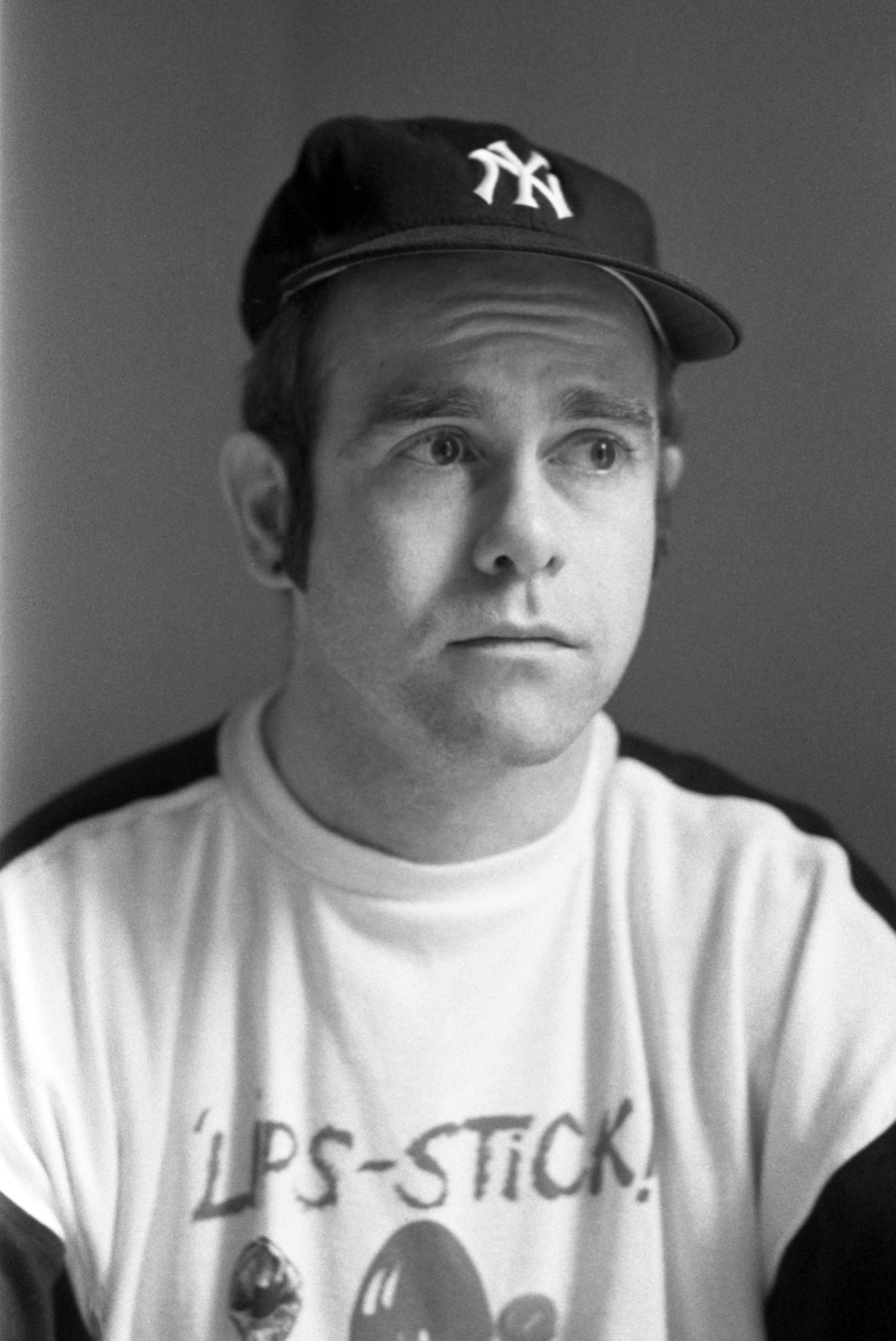Elton John wearing a New York Yankees cap and a graphic T-shirt