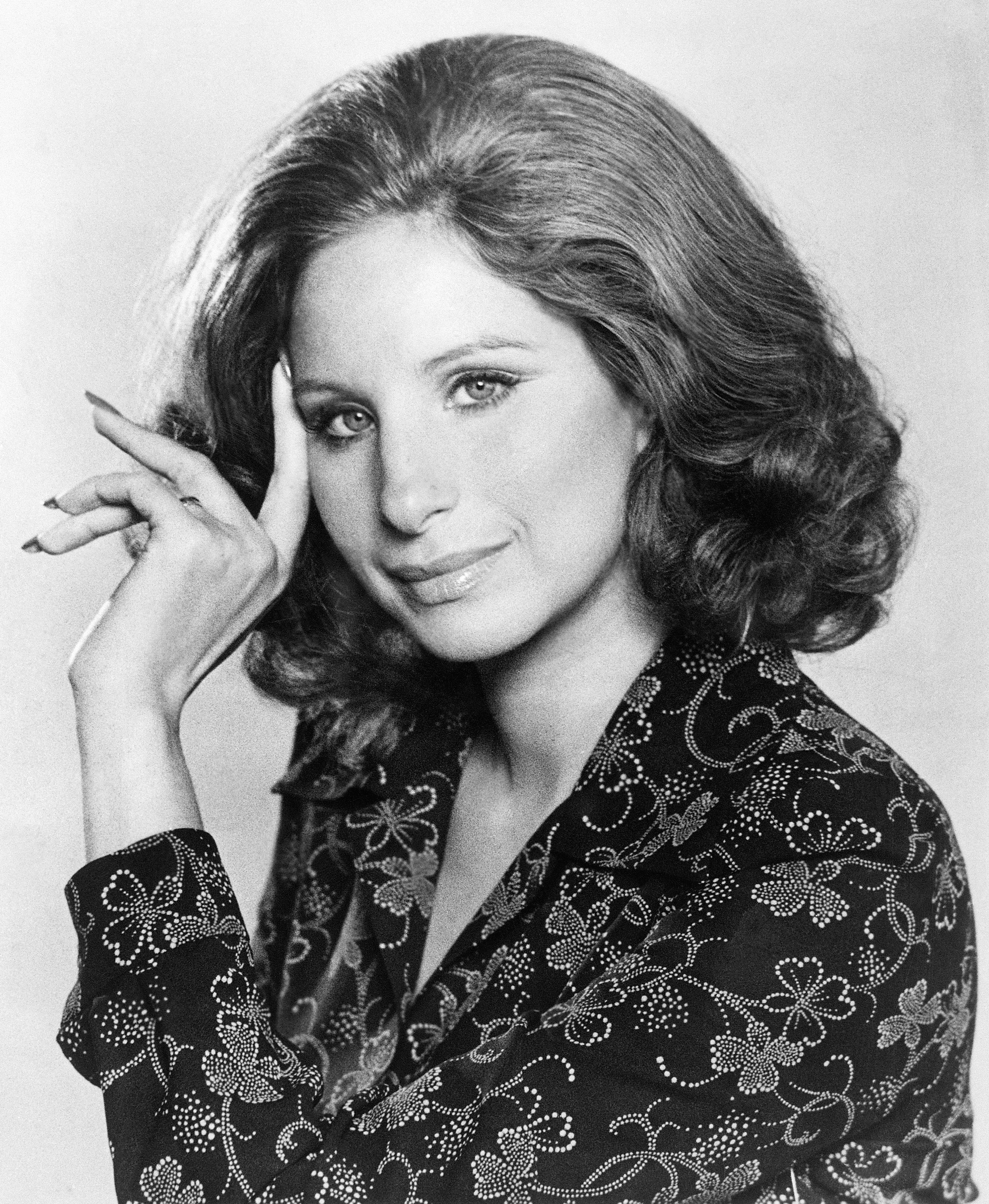 Barbra Streisand poses with a hand to her temple, wearing a patterned jacket