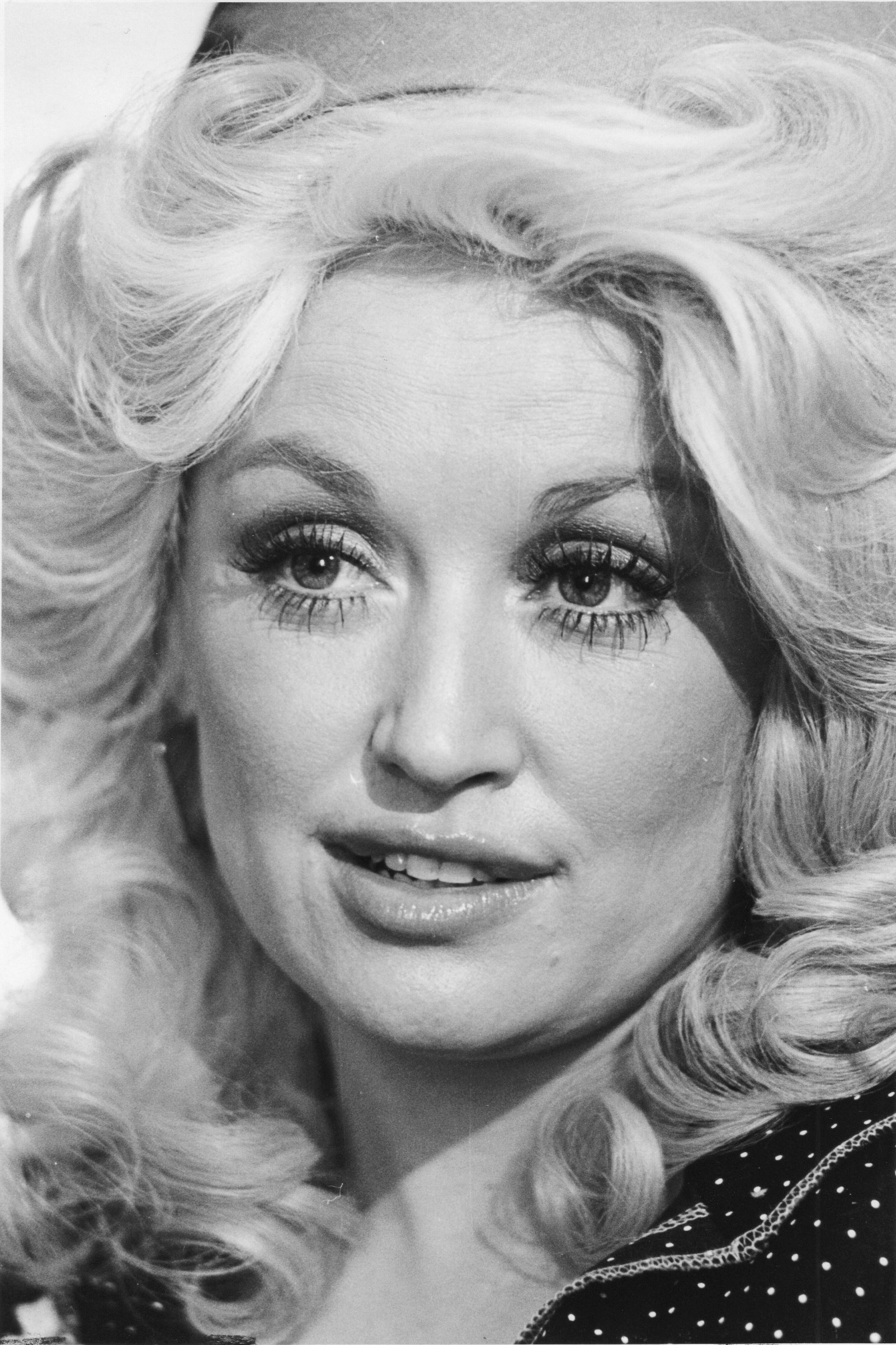 Dolly Parton with voluminous curly hair and detailed eye makeup, looking slightly to the side