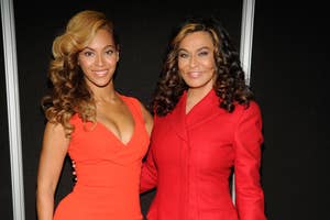Beyoncé, in a form-fitting dress, stands next to Tina Knowles, wearing a jacket and black pants. Both are smiling and posed for a photo