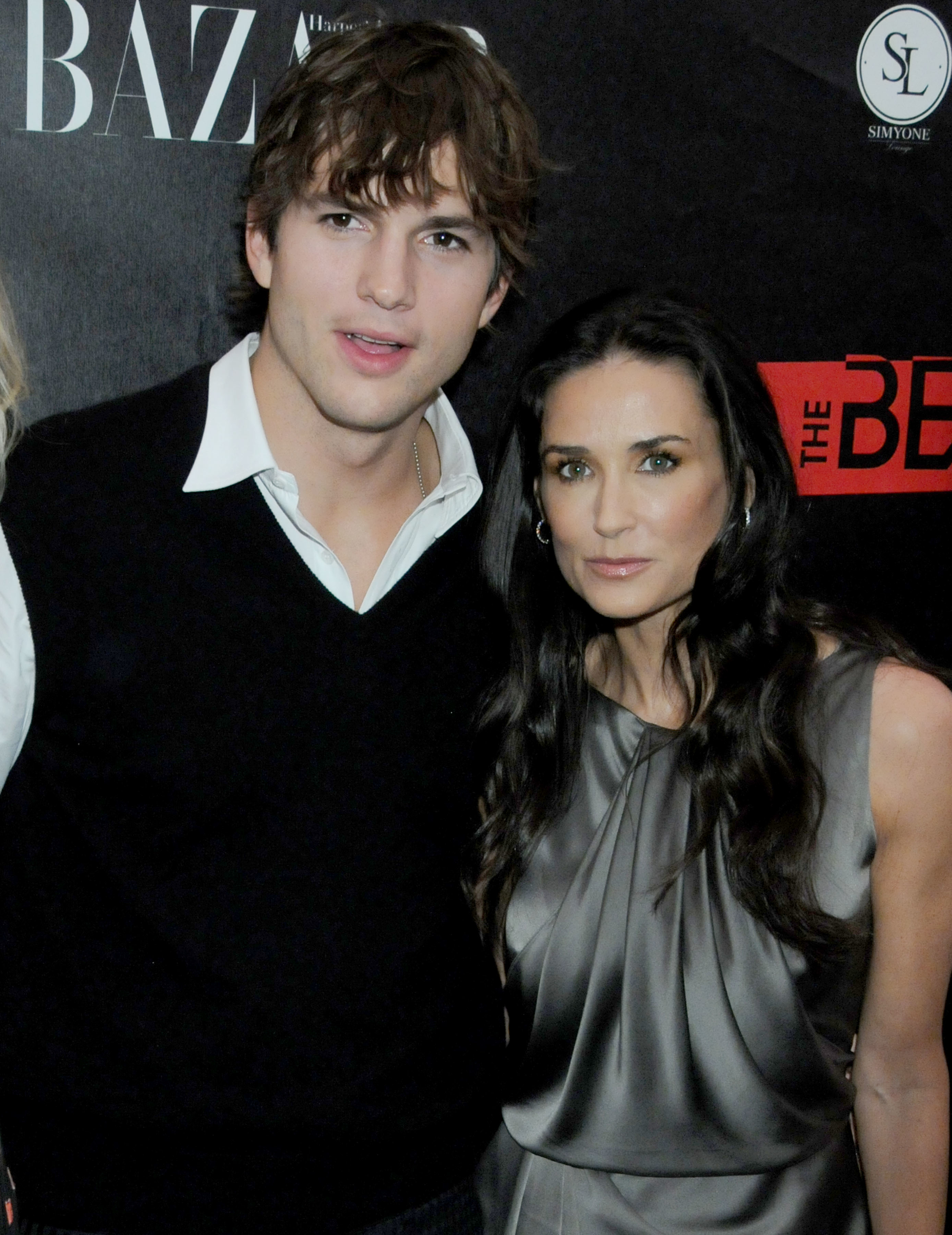 Ashton Kutcher and Demi Moore at a Harper's Bazaar event, with Ashton wearing a sweater over a collared shirt and Demi in a sleeveless dress
