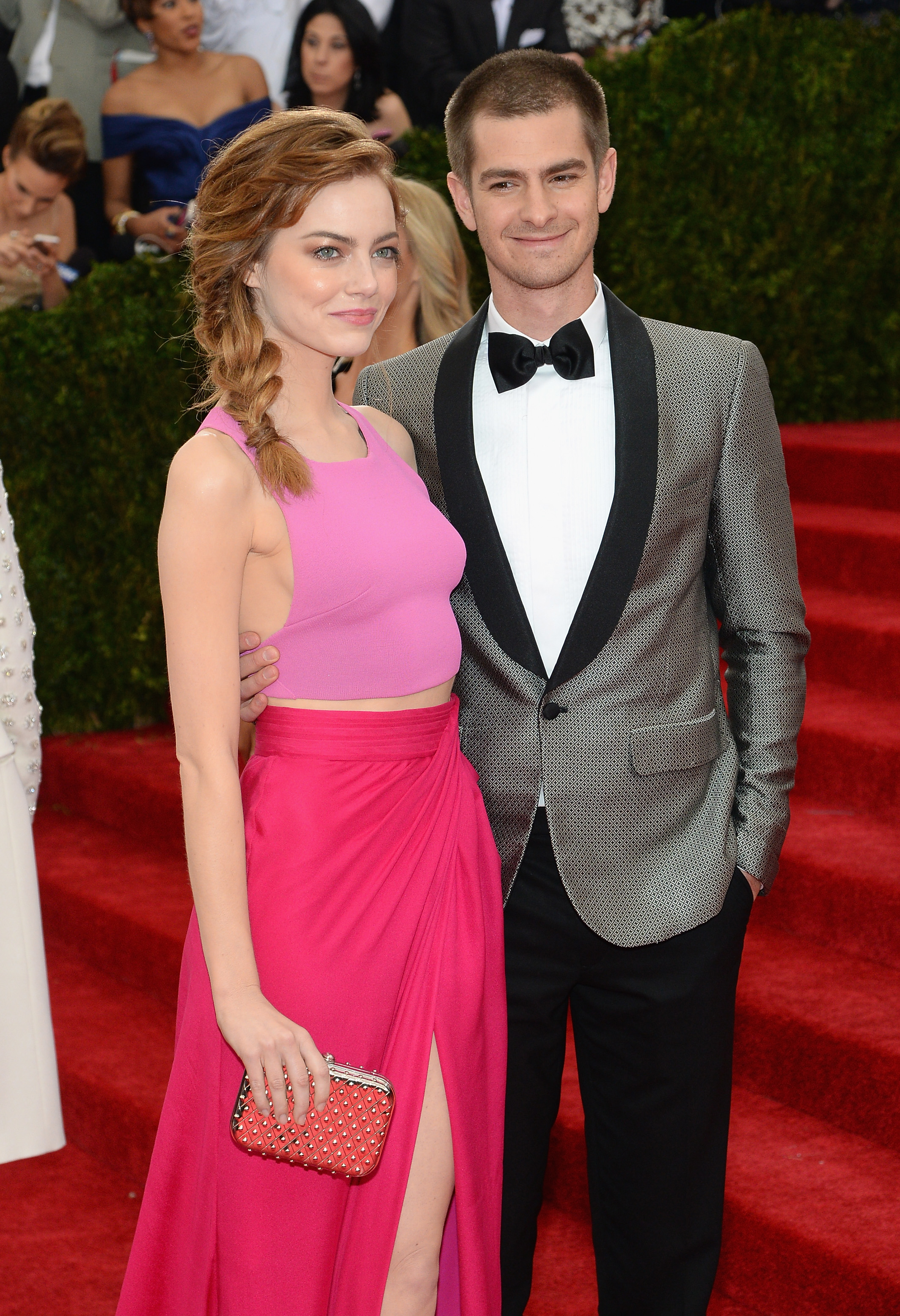 Emma Stone in a sleeveless pink top and high-slit skirt, and Andrew Garfield in a suit with a bow tie, pose together on a red carpet