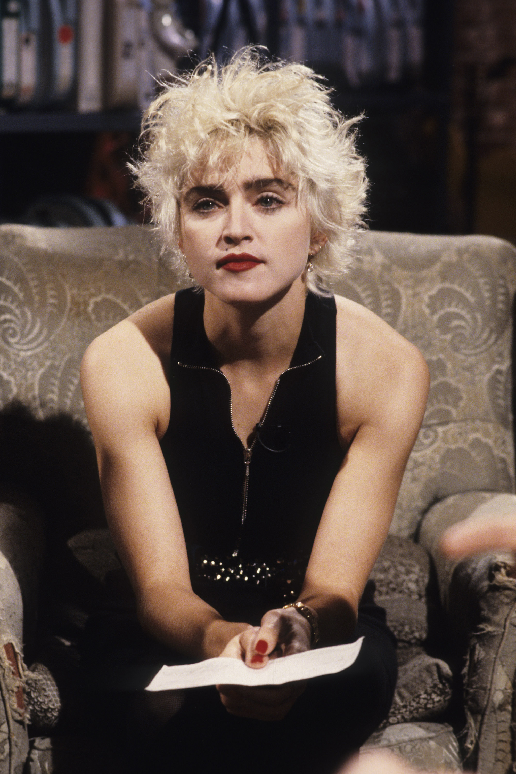 Madonna sitting on a chair, wearing a sleeveless black top and holding a piece of paper