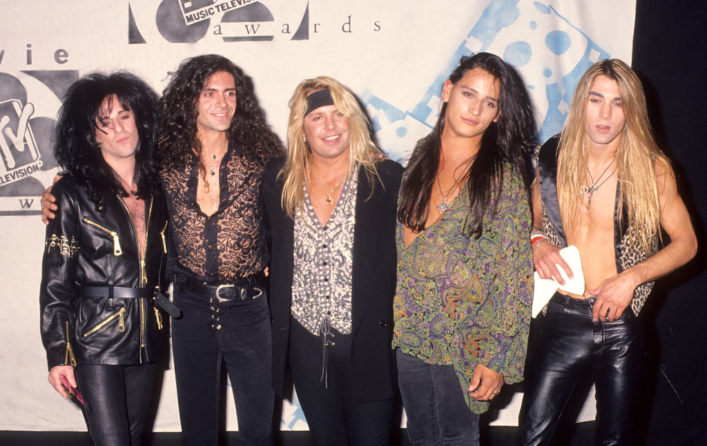 Motley Crue band members stand together at an MTV music awards event, dressed in their signature rock attire with leather jackets and patterned shirts