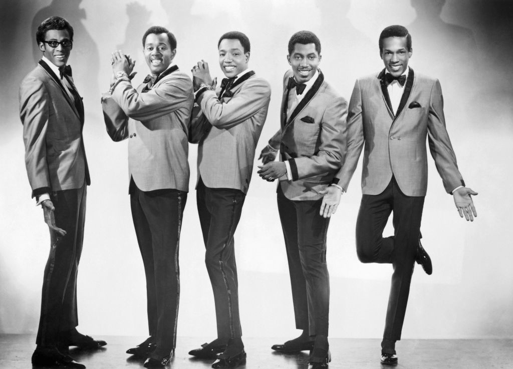 Five members of The Temptations stand in matching suits, smiling and posing