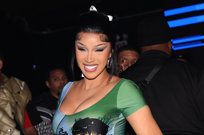 Cardi B smiles while wearing a graphic-print top at an event, surrounded by people