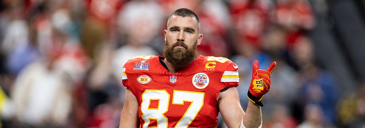 NFL player Travis Kelce in a red Kansas City Chiefs jersey with number 87, holding up two fingers on a stadium field during a game