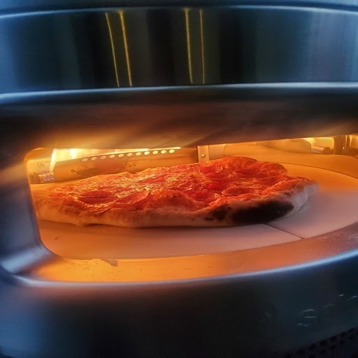A pepperoni pizza is baking inside an oven, with the crust starting to brown and cheese melting under the heat