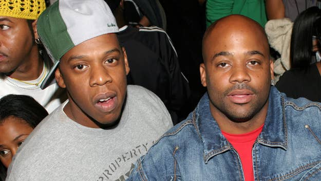 Two people, Jay-Z and Damon Dash, are standing side by side at an event. Jay-Z is wearing a casual t-shirt and a backward cap, while Damon Dash is in a denim jacket
