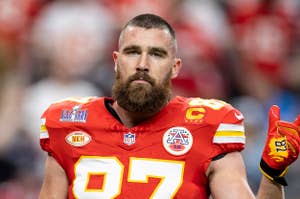 NFL player Travis Kelce in a red Kansas City Chiefs jersey with number 87, holding up two fingers on a stadium field during a game