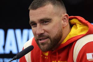 Travis Kelce speaks at a press conference, wearing a Chiefs-themed hoodie with "Kelce" on the sleeve