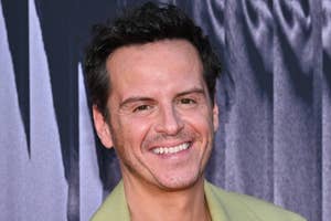 Andrew Scott smiling at the camera in front of a patterned background