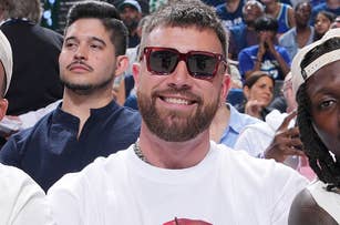 Patrick Mahomes, Travis Kelce, and Kadarius Toney sit courtside at a basketball game, each wearing casual stylish outfits, with a crowd in the background