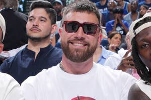 Patrick Mahomes, Travis Kelce, and Kadarius Toney sit courtside at a basketball game, each wearing casual stylish outfits, with a crowd in the background