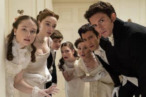 Bridgerton cast in period costumes gathered closely, looking with surprise: Florence Hunt, Phoebe Dynevor, Luke Newton, Claudia Jessie, Ruth Gemmell, Luke Thompson, Jonathan Bailey