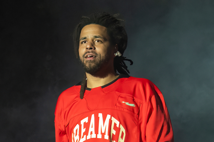 J. Cole looks ahead while performing on stage, wearing a jersey with "Dreamer" written on it