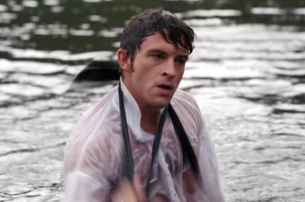 Jonathan Bailey is emerging from the water, wearing a wet white shirt partially unbuttoned, and holding black suspenders as Anthony on Bridgerton