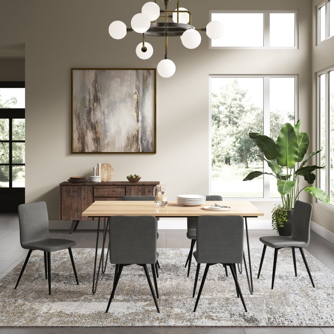 Dining room with a wooden table, five grey chairs, an abstract painting on the wall, plant, and a modern chandelier. Large windows provide sunshine.
