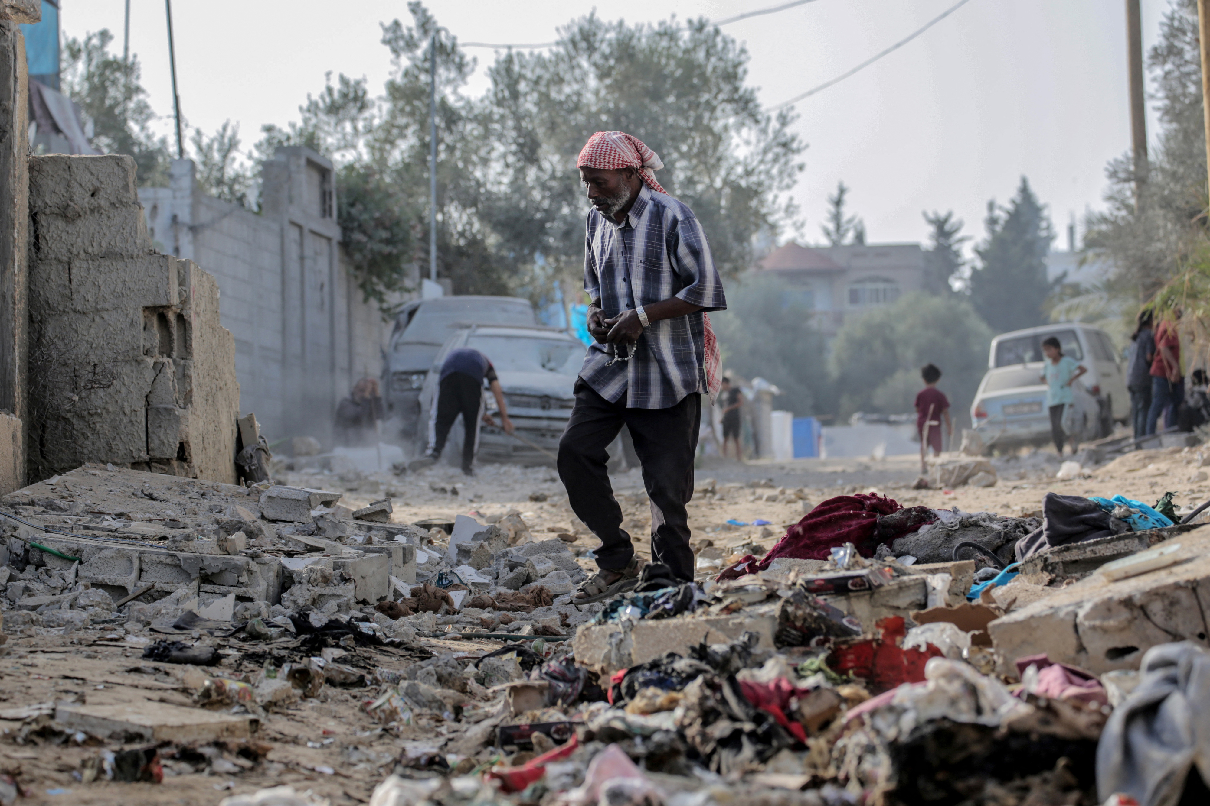 A man walks through rubble and debris on a damaged street, with buildings and vehicles around him in a scene suggesting aftermath of destruction