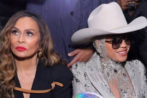 Tina Knowles and Beyoncé attend a fashion event. Tina wears a black outfit with brown gloves, and Beyoncé is in a metallic suit with an embellished hat and a large iridescent bag